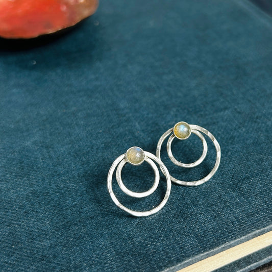 Two small concentric circles handmade in hammered silver make each of these stud earrings, with a small labradorite cabochon at the top of each earring.  Sat catching the light on an old blue book