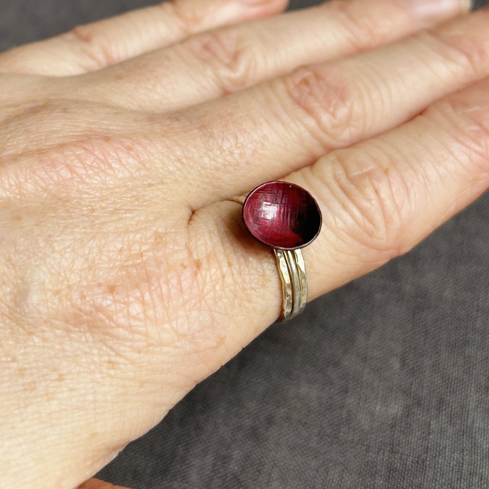 Hand wearing a ring with a red copper circle and silver band on a neutral background