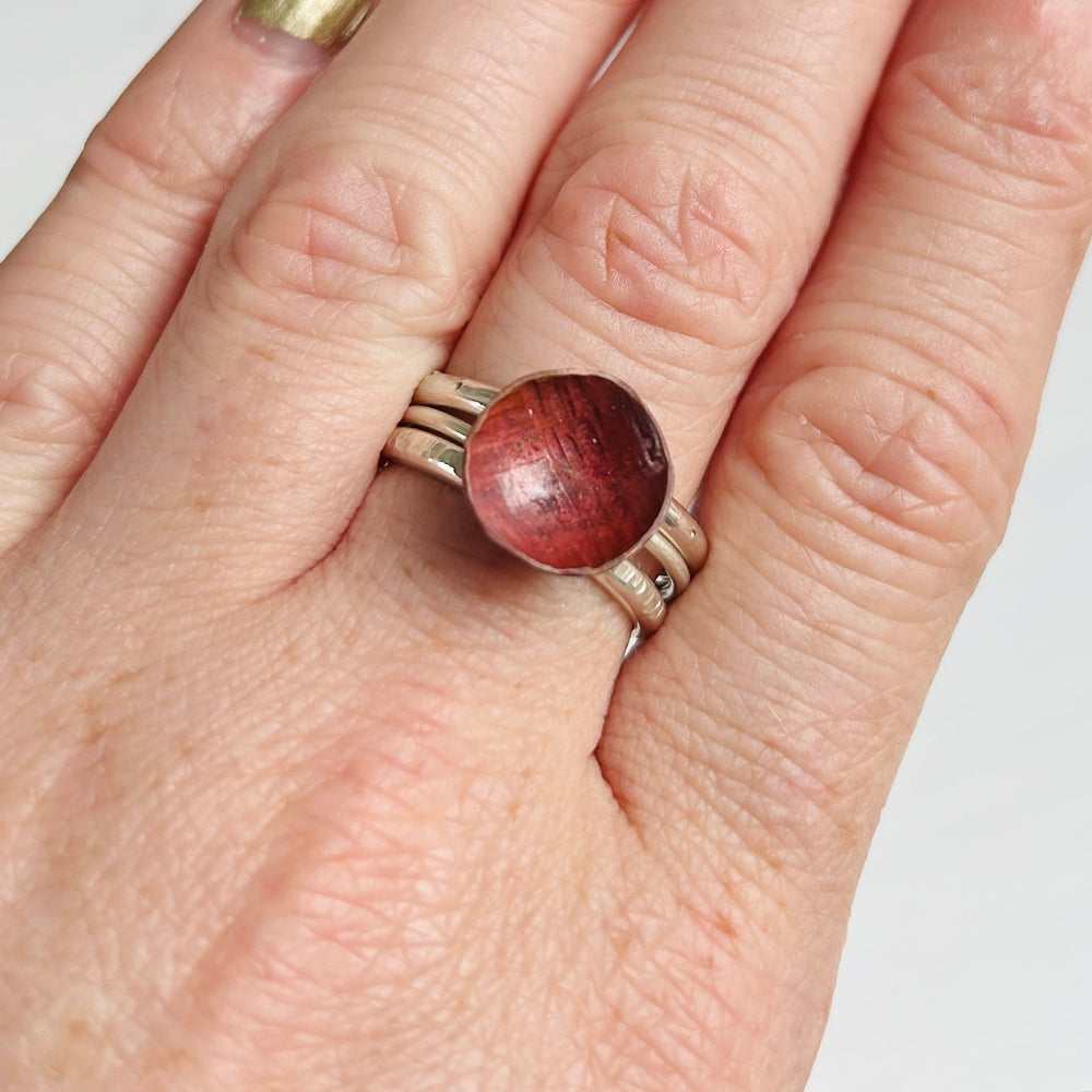 Hand wearing a ring with a red copper circle on a plain background