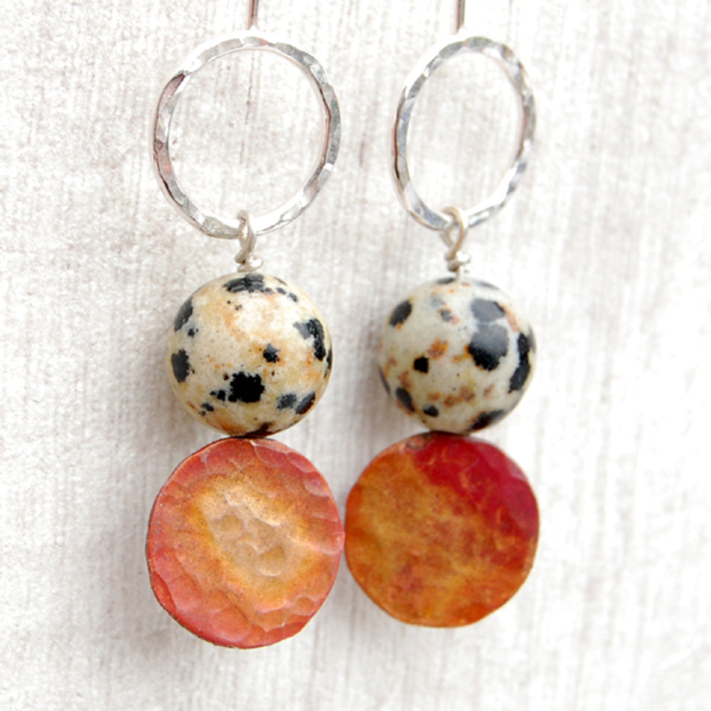 Close up of silver hook style earrings with an open silver circle at the top, a natural Jasper Dalmation stone, then a coloured copper disk below, by zoe ruth designs