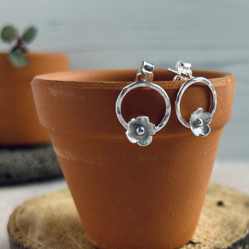 Two stud earrings, each with one sterling silver 5 petal flowers, hammered on the petals and with 3D silver ball centres, attached to the bottom of a small open circle, stud attached at the top, by zoe ruth designs
