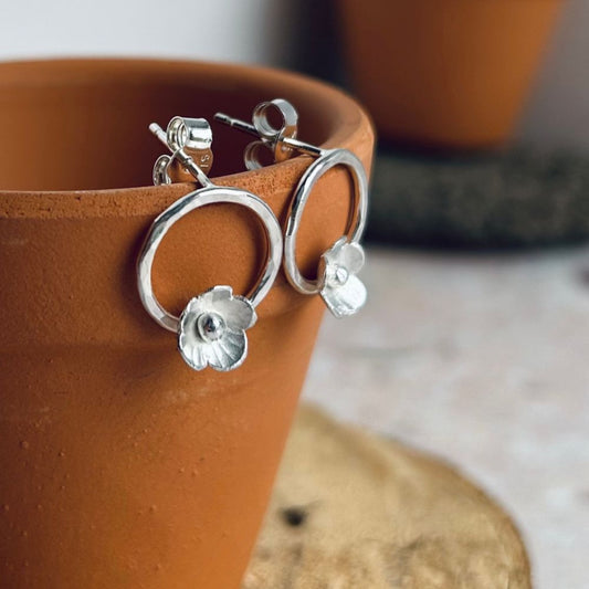 Two stud earrings, each with one sterling silver 5 petal flowers, hammered on the petals and with 3D silver ball centres, attached to the bottom of a small open circle, stud attached at the top, by zoe ruth designs