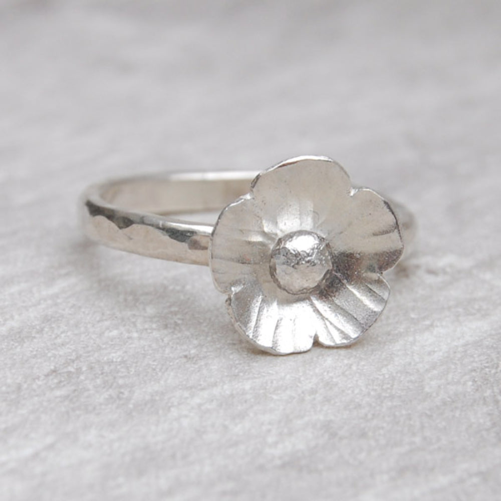 A five petaled silver flower sits on a hammered silver slim ring, by zoe ruth designs