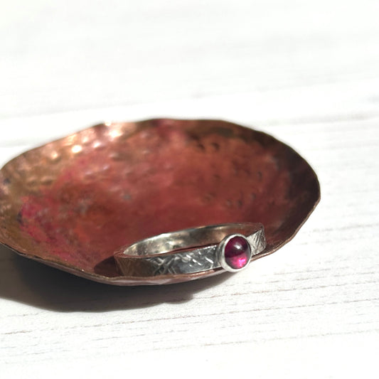 Showing the deep red of a garnet stone on a textured handmade silver ring