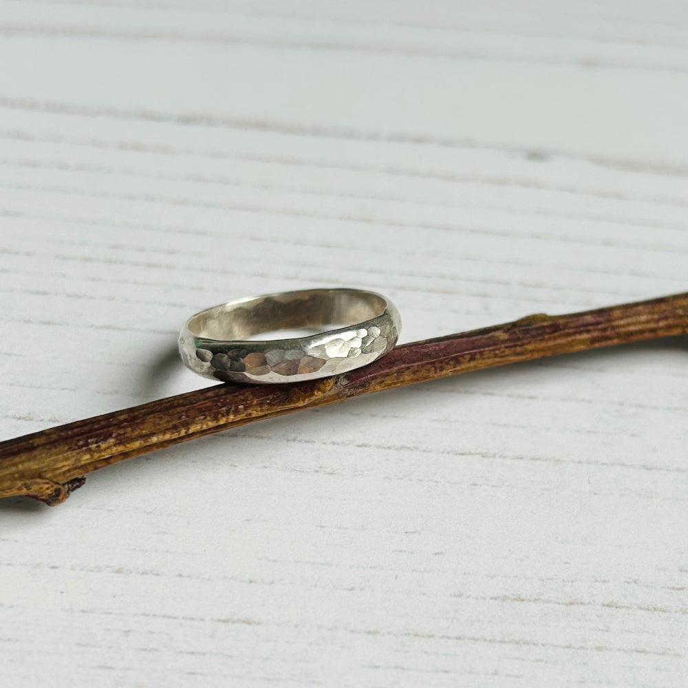 A classic dimple hammer texture on a D profile silver ring, sat tilted towards the light on a garden twig, by zoe ruth designs