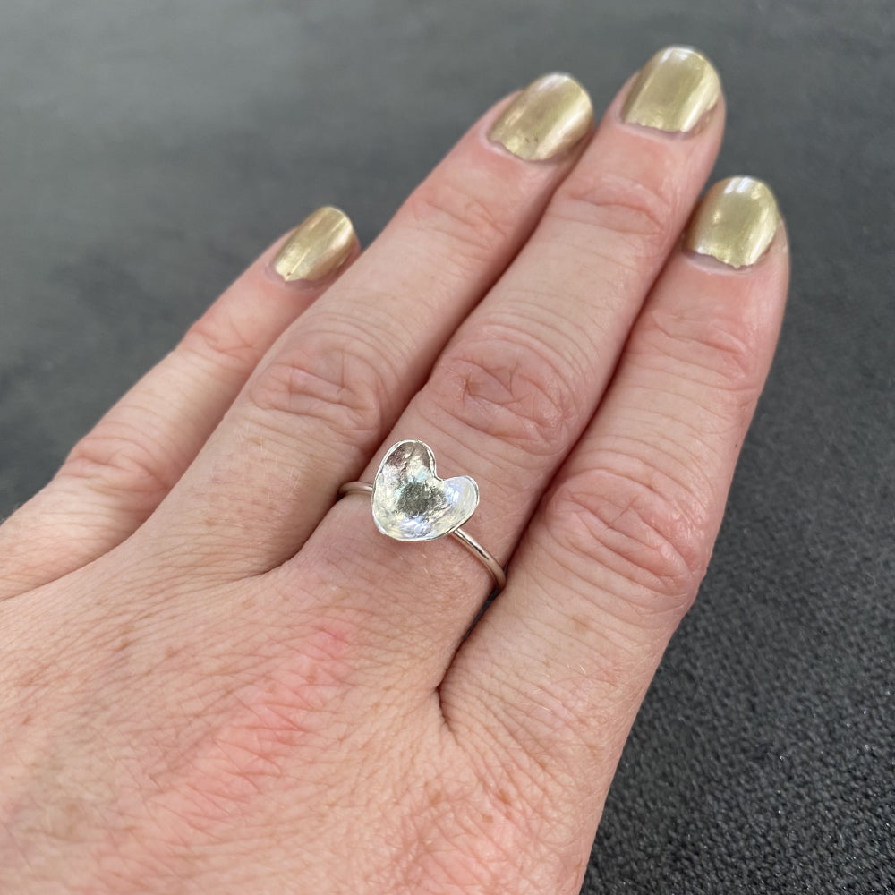Hammered silver heart on a thin round silver wire ring being worn, by zoe ruth designs