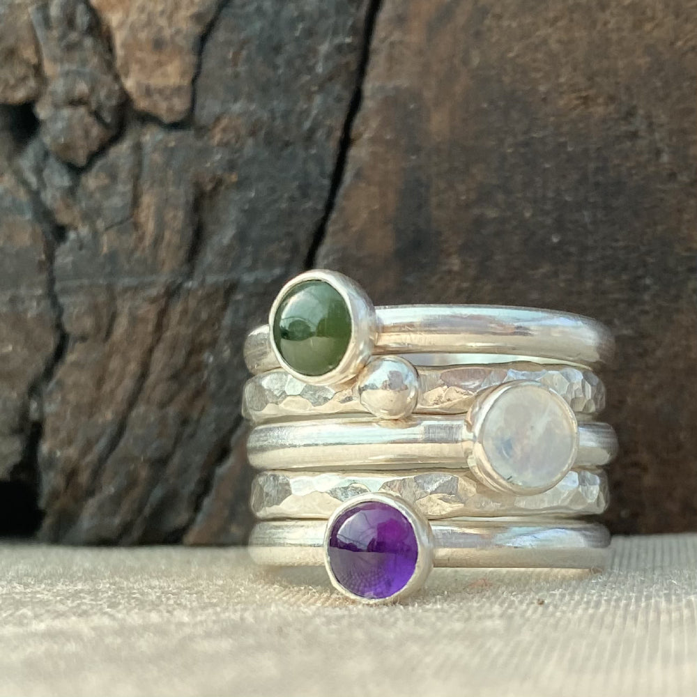 A set of five rings, one a textured silver band,one textured with a silver pebble, one smooth with a green jade, one smooth with a whiteish clear moonstone, one smooth with a purple amethyst, by zoe ruth designs