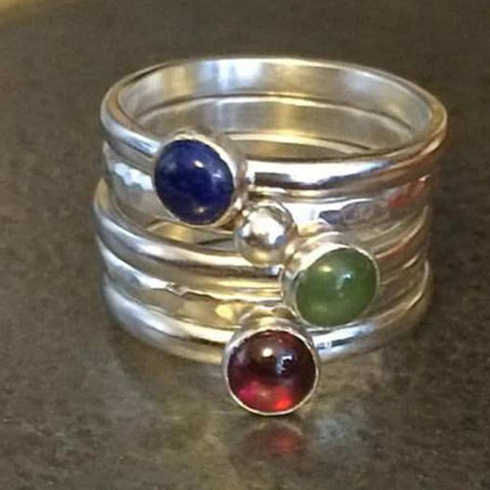 A set of five rings, one a textured silver band,one textured with a silver pebble, one smooth with a green jade, one smooth with a red garnet, one smooth with a blue lapis lazuli, by zoe ruth designs