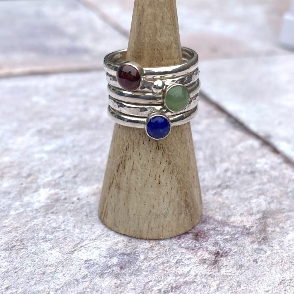 A set of five rings, one a textured silver band,one textured with a silver pebble, one smooth with a green jade, one smooth with a red garnet, one smooth with a blue lapis lazuli, by zoe ruth designs