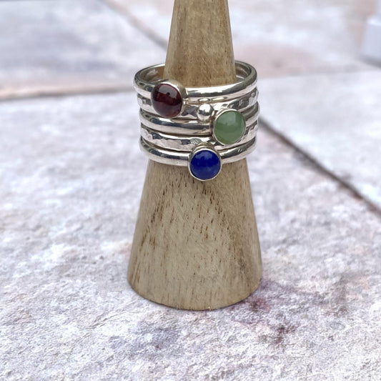 A set of five rings, one a textured silver band,one textured with a silver pebble, one smooth with a green jade, one smooth with a red garnet, one smooth with a blue lapis lazuli, by zoe ruth designs