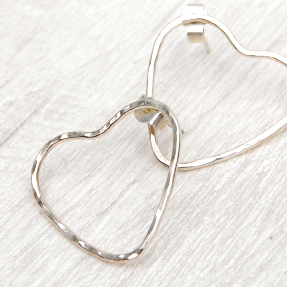 Two silver heart stud earrings, made from hammered wire to give the outline of hearts, the earring stud placed on opposing sides, by zoe ruth designs
