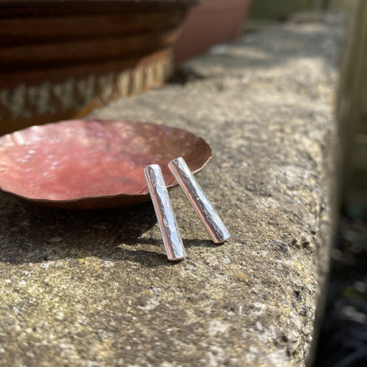 long slim rectangles of half rounded silver wire hammered make these earring studs, displayed on a copper dish outside, by zoe ruth designs
