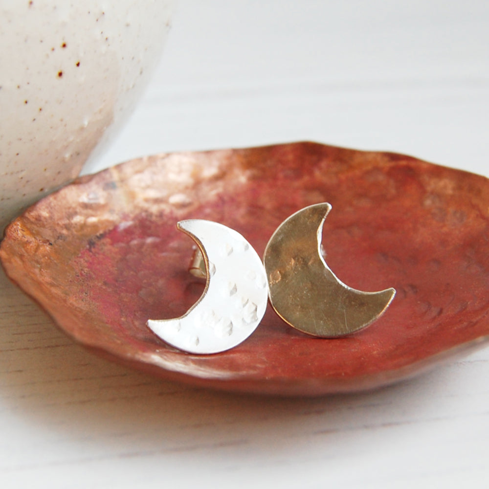 A pair of hand sawn and textured sterling silver crescent moon shaped stud earrings, sat in a copper dish, by zoe ruth designs
