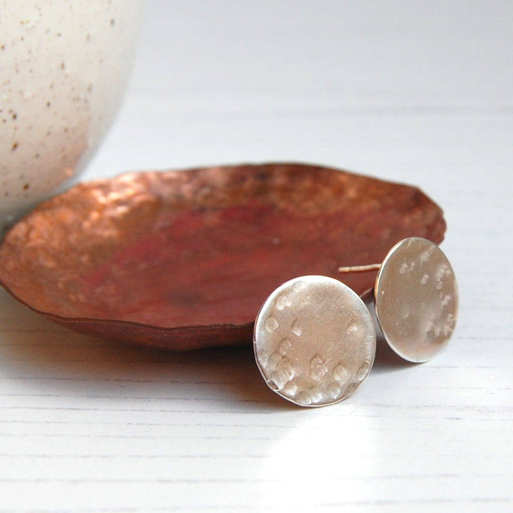 A pair of silver disk shaped stud earring with some gentle hammer marks to suggest craters on a full moon surface, by zoe ruth designs