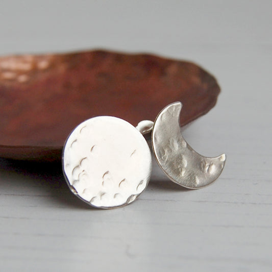 A pair or silver stud earrings, one a full moon with some hammered marks and one a crescent moon with some hammered marks, by zoe ruth designs.
