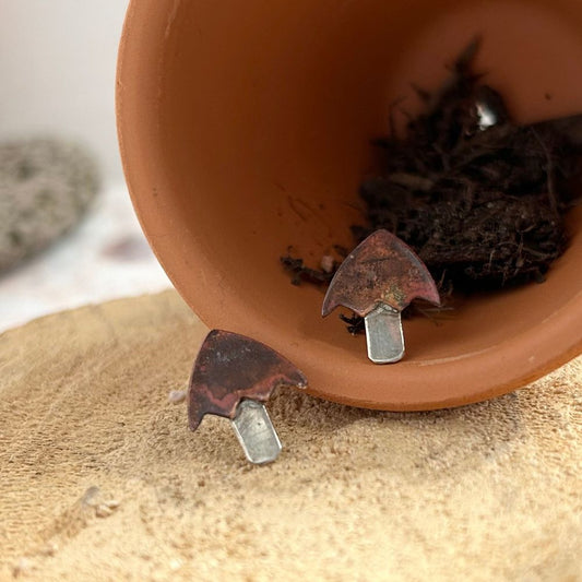 A pair of mushroom shaped earrings with copper tops and silver stalks are shown sat on a small terracotta pot with soil, by zoe ruth designs