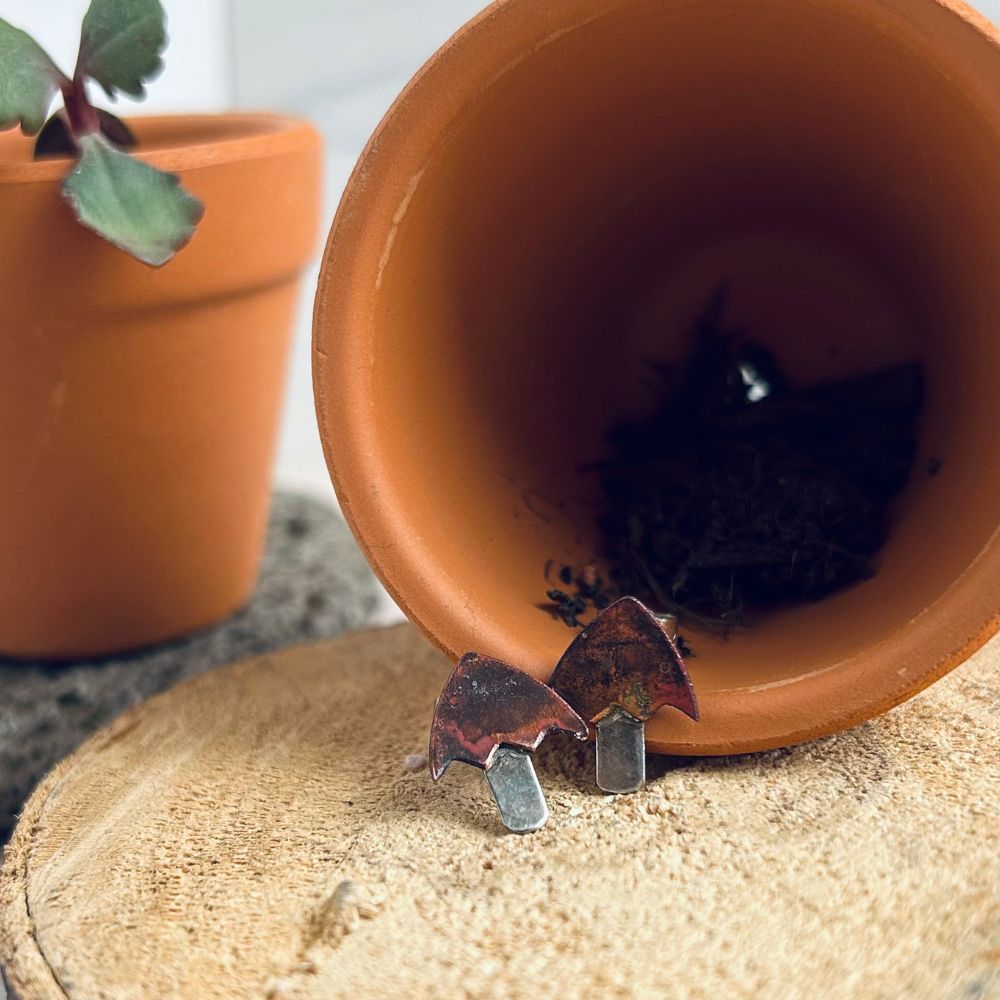 A pair of mushroom shaped earrings with copper tops and silver stalks are shown sat in front of a small terracotta pot, by zoe ruth designs