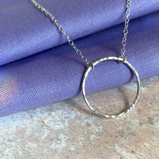 A slim circle frame pendant, sterling silver and lightly hammered, hangs from a sterling silver chain, shown catching the light, by zoe ruth designs.