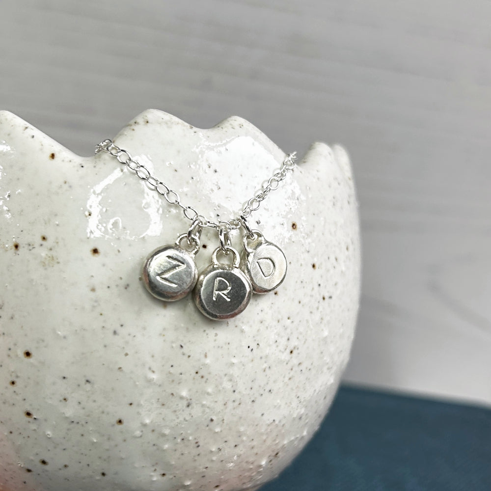 Showing a personalised letter stamped necklace by zoe ruth designs with three letter stamped silver charm pebbles.