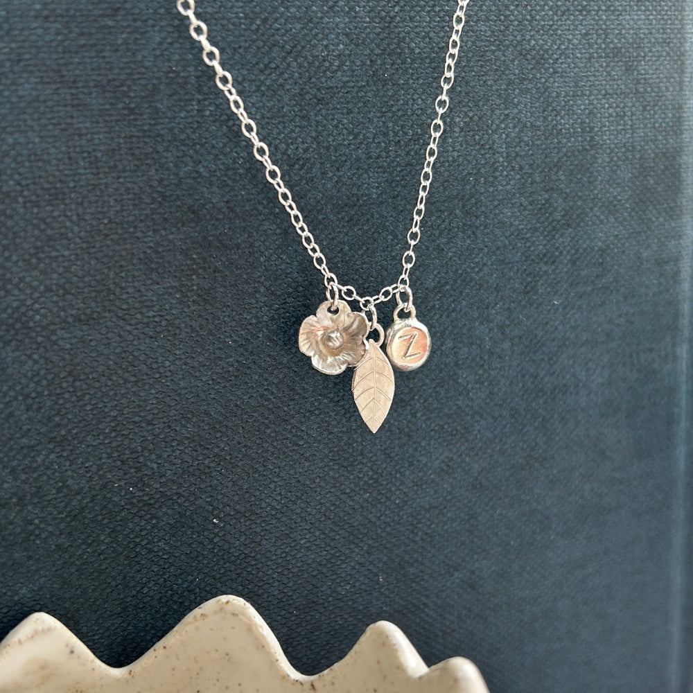 Silver charm necklace with a handmade silver flower, silver leaf, personalised letter stamped silver pebble by zoe ruth designs
