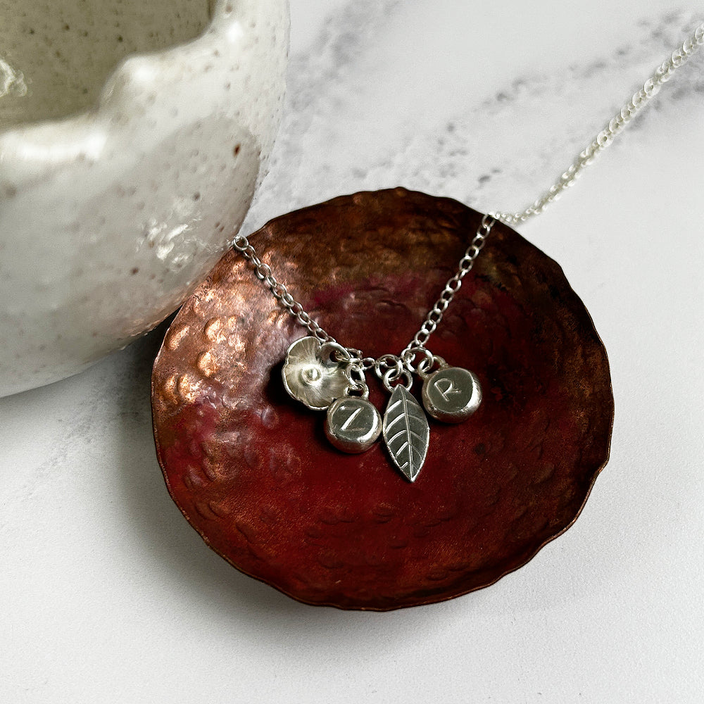 Silver charm necklace showing a handmade silver flower, leaf, and two silver pebble charms stamped with letters Z and R, by zoe ruth designs