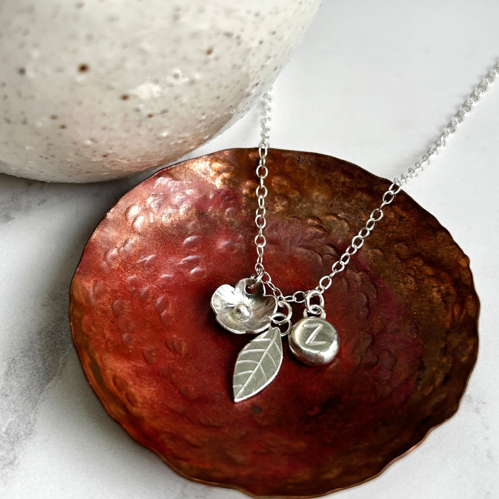 Silver flower, silver leaf, silver pebble with personalised letter stamped on hanging as charms from a necklace by zoe ruth designs