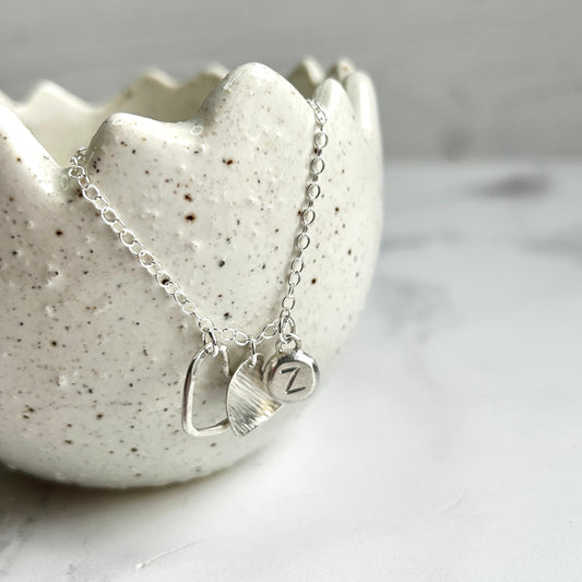two delicate handmade silver hearts and a silver pebble with letter Z hanging as charms from a silver chain, by zoe ruth designs