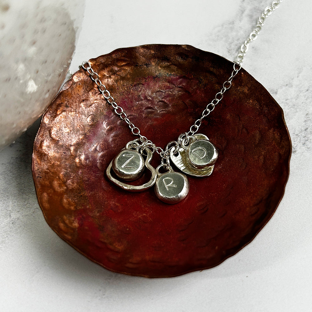 Necklace of handmade silver hearts and three silver pebbles with the letter Z, letter R, and letter D stamped  on them, by zoe ruth designs