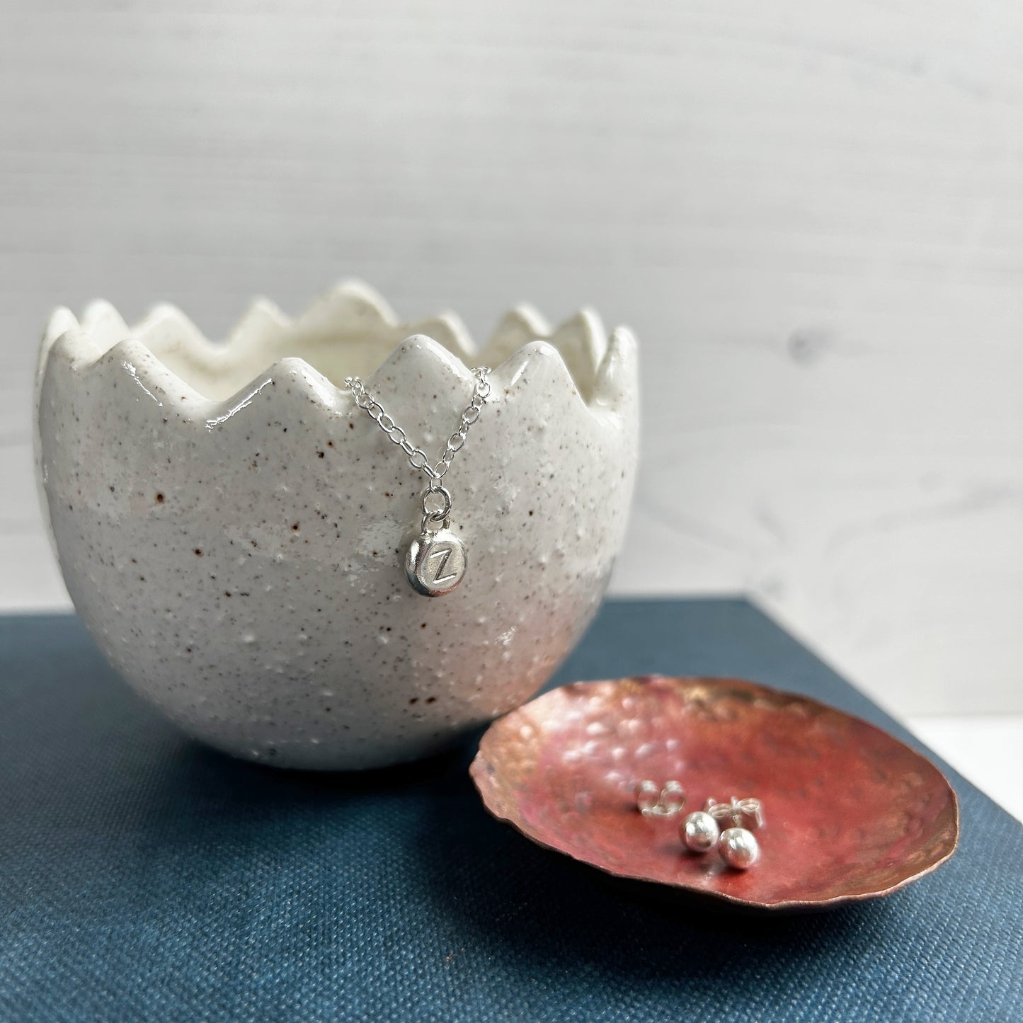 This photo shows a silver necklace and silver earrings, the necklace has a charm with a letter on it and the earrings are rounded pebbles, by zoe ruth designs