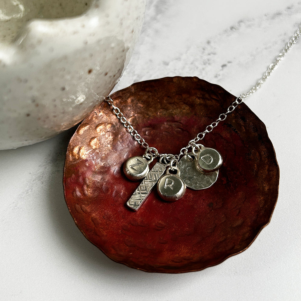 Silver charms necklace with a textured bar, disk and three silver pebble charms with  letters Z, R and D by zoe ruth designs