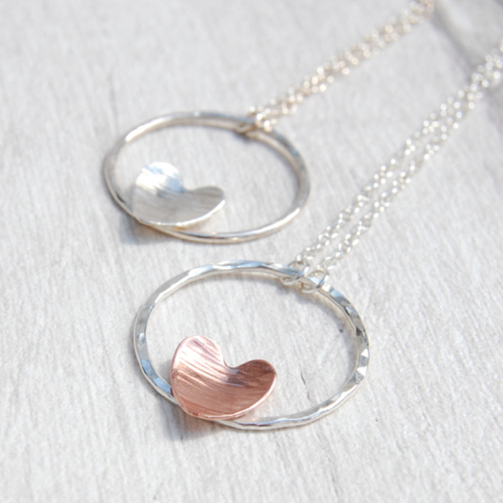 A textured copper heart and silver circle necklace next to a silver heart and circle necklace, designed and made by zoe ruth designs