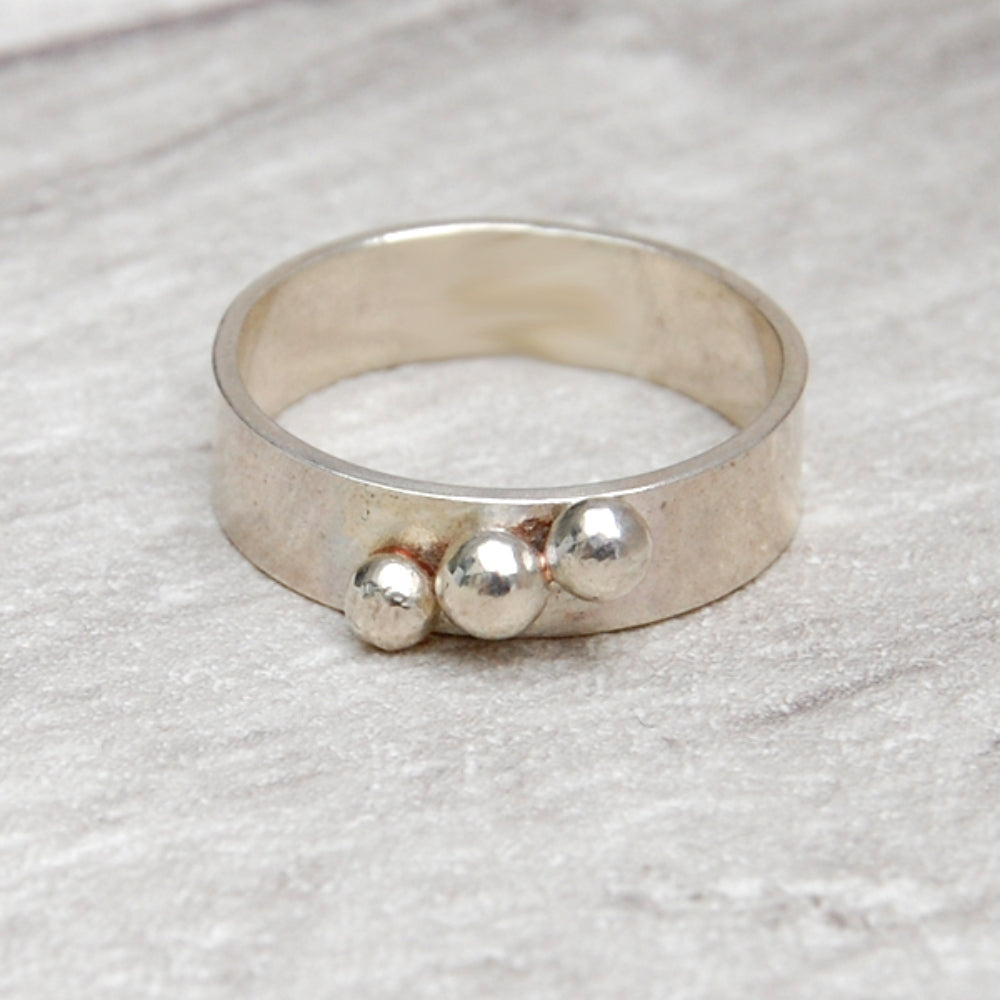 A 5mm wide smooth silver band with three silver balls soldered in a diagonalline across the width, b  zoe ruth designs.