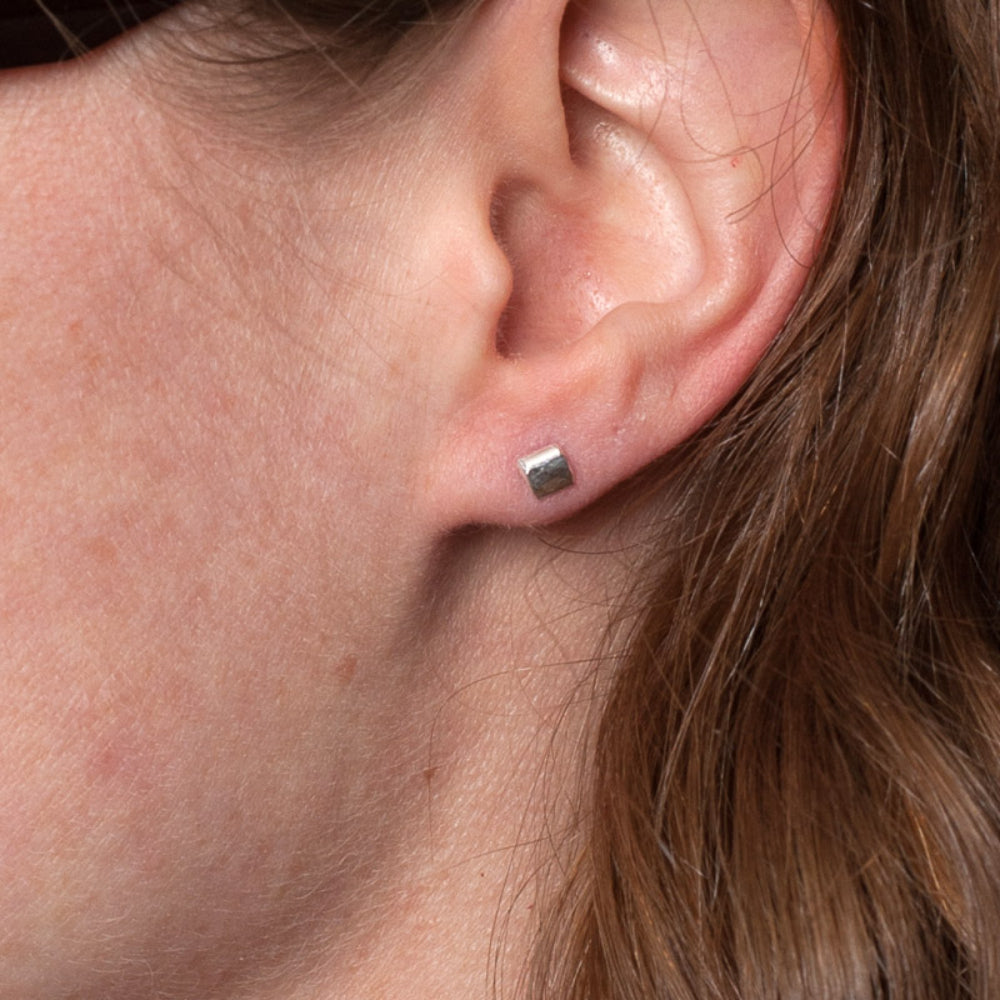 a pair of small silver square hammered stud earrings being worn by zoe ruth designs.