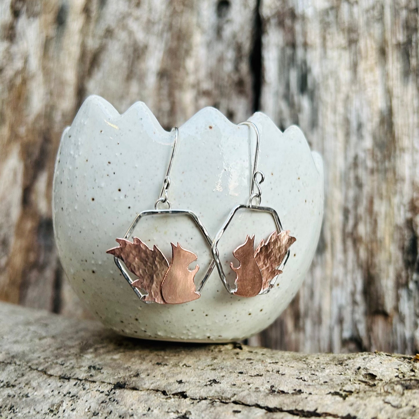 Earrings made from handsawn copper squirrel 2D in profile, smooth body and hammered tail. sat on sterling silver hexagon frame, hanging from silver hooks, by zoe ruth designs