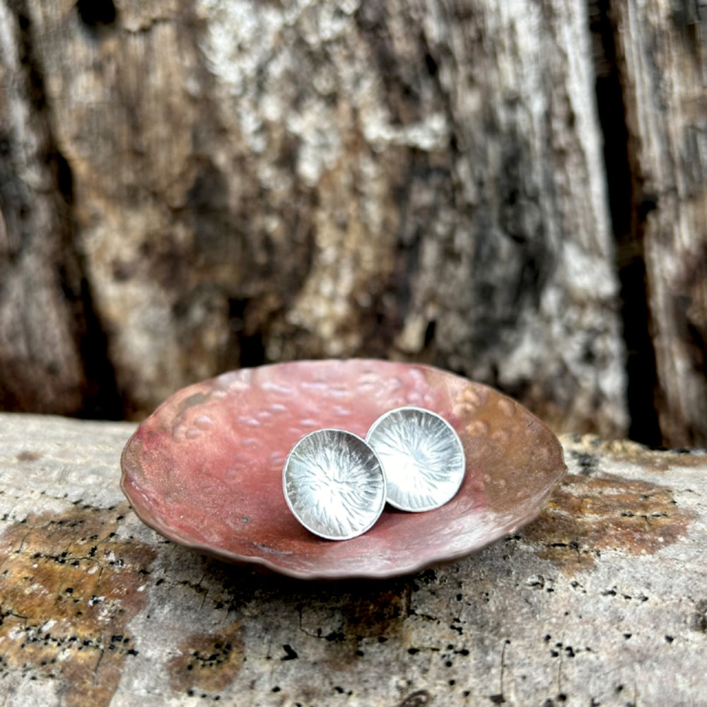 Silver stud earrings,  each one a softly concave silver disk with a radial lines texture, sat in a copper dish, by zoe ruth designs.