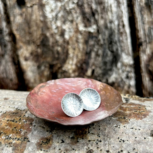Silver stud earrings,  each one a softly concave silver disk with a radial lines texture, sat in a copper dish, by zoe ruth designs.