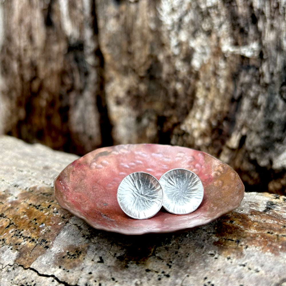 Silver stud earrings,  each one a softly concave silver disk with a radial lines texture, sat in a copper dish, by zoe ruth designs.