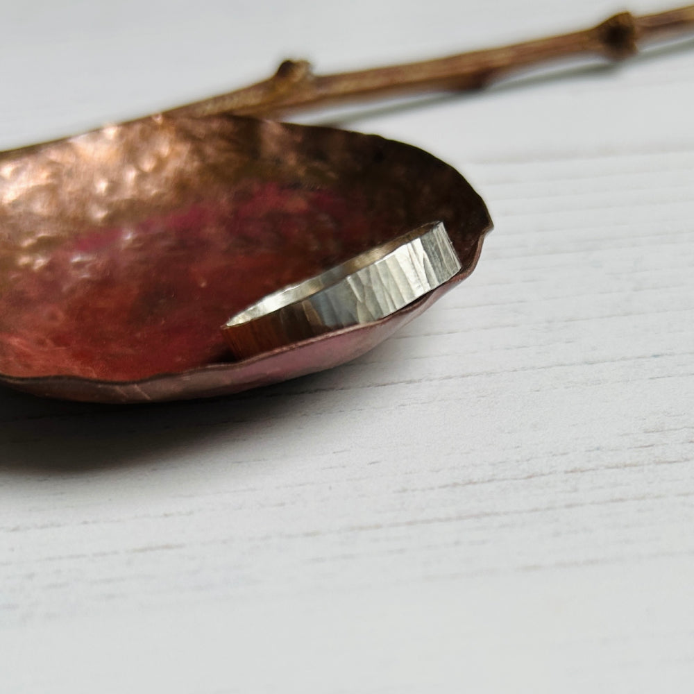 A 5mm wide silver ring with a linear treebark like texture, by zoe ruth designs.