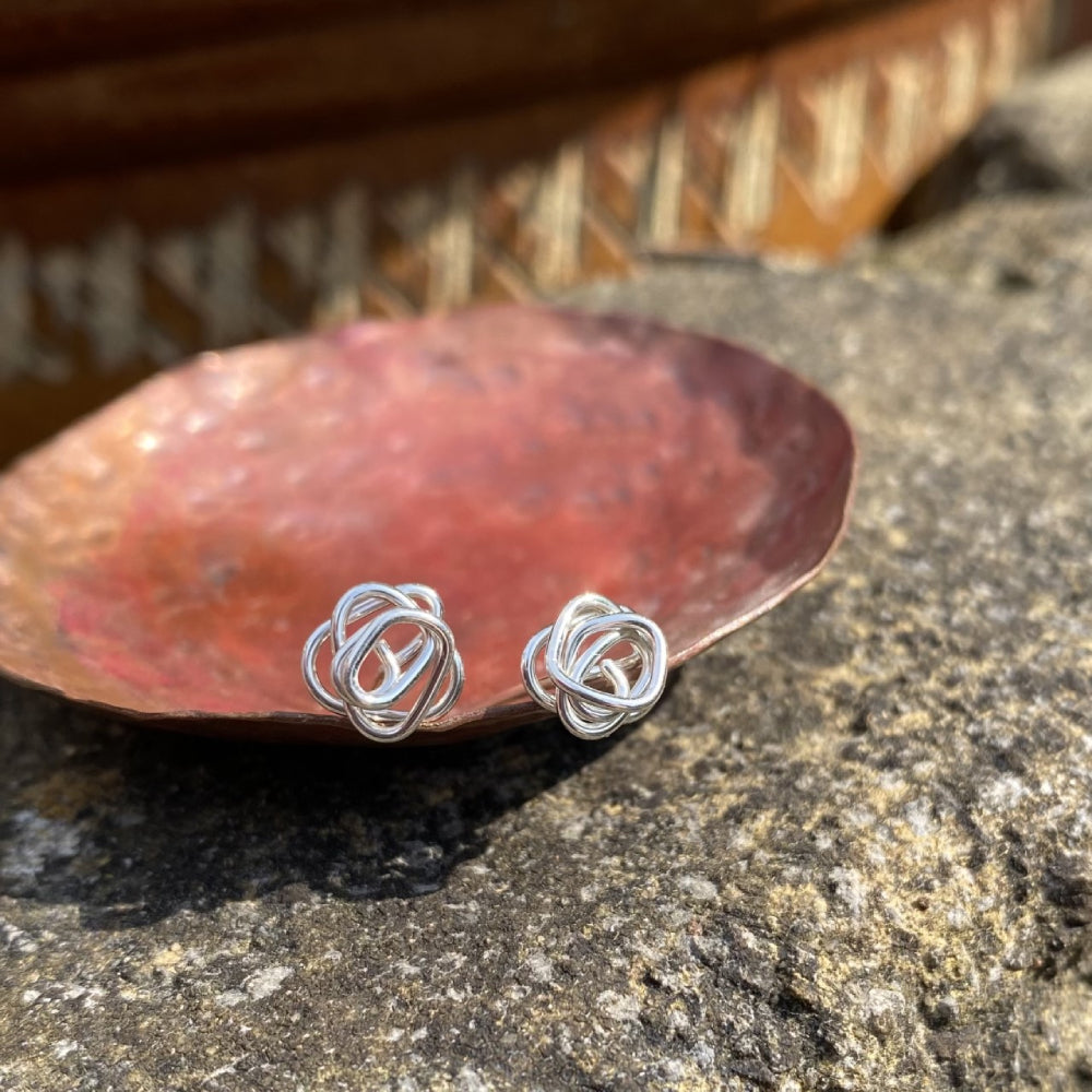 A pair of silver stud earrings each made from a messy coil of sterling silver wire, sat in a copper dish, by zoe ruth designs.