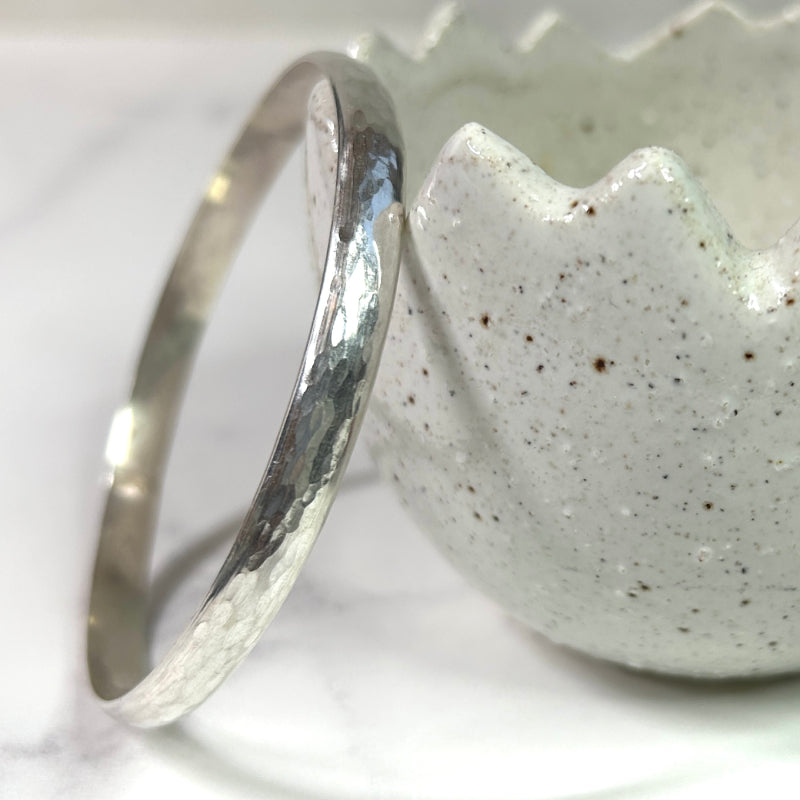 A chunky handmade silver bangle showing texture marks and shine