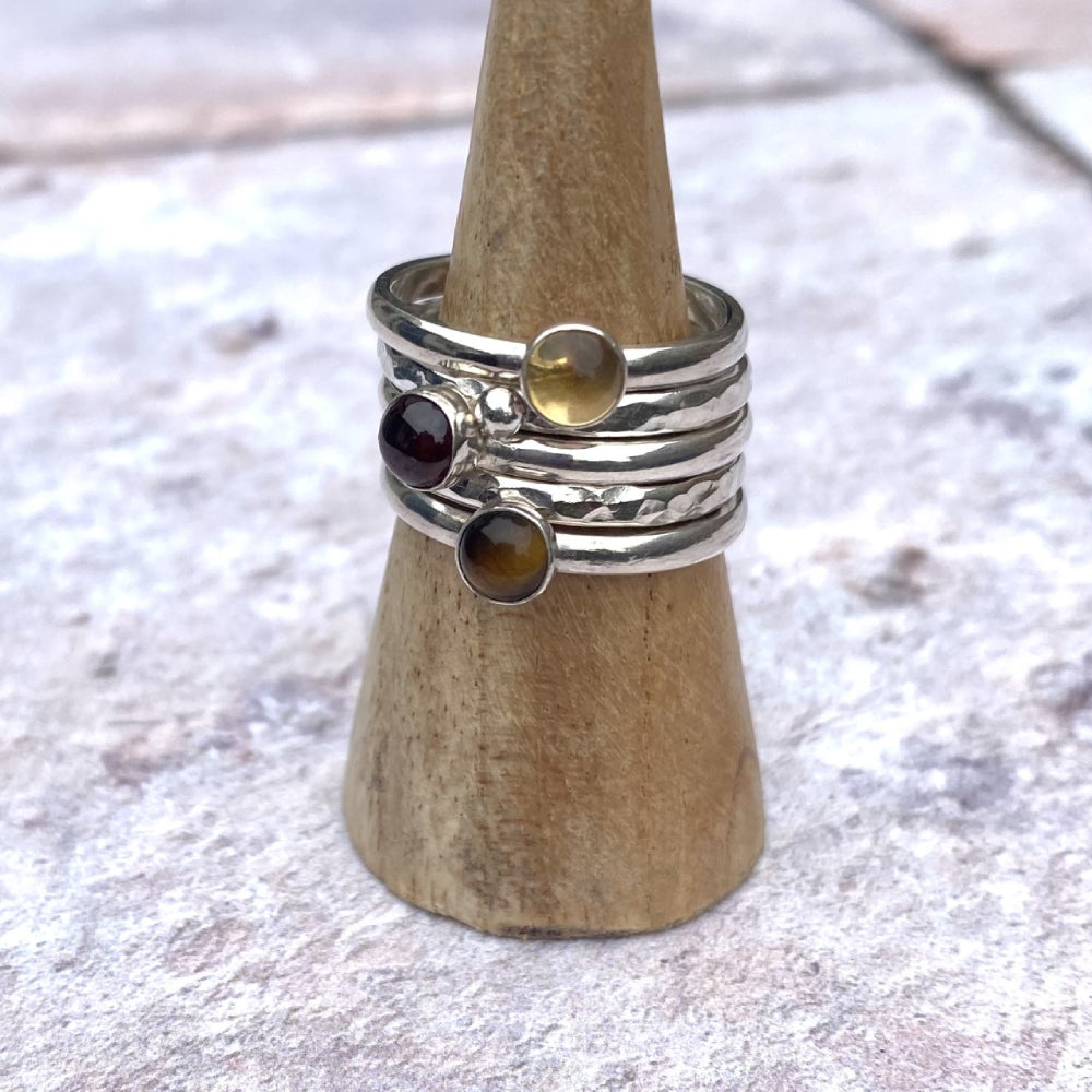 A set of five rings, one a textured silver band,one textured with a silver pebble, one smooth with a brown tigers eye, one smooth with a red garnet, one smooth with a yellow citrine, by zoe ruth designs