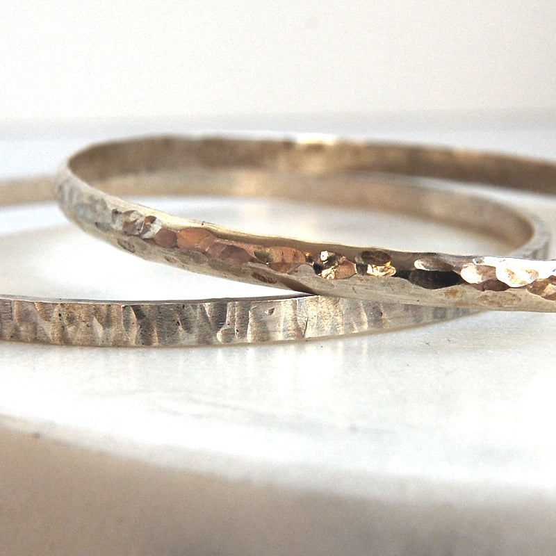 Showing two silver bangles with different textures, one a classic dimple textured surface the other a linear hammered texture, by zoe ruth designs