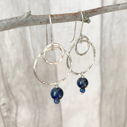 Showing handmade silver hook earrings, each with a double silver circle outline, the smaller layered over the larger, with two Lapis Lazuli stones hanging underneath, by zoe ruth designs