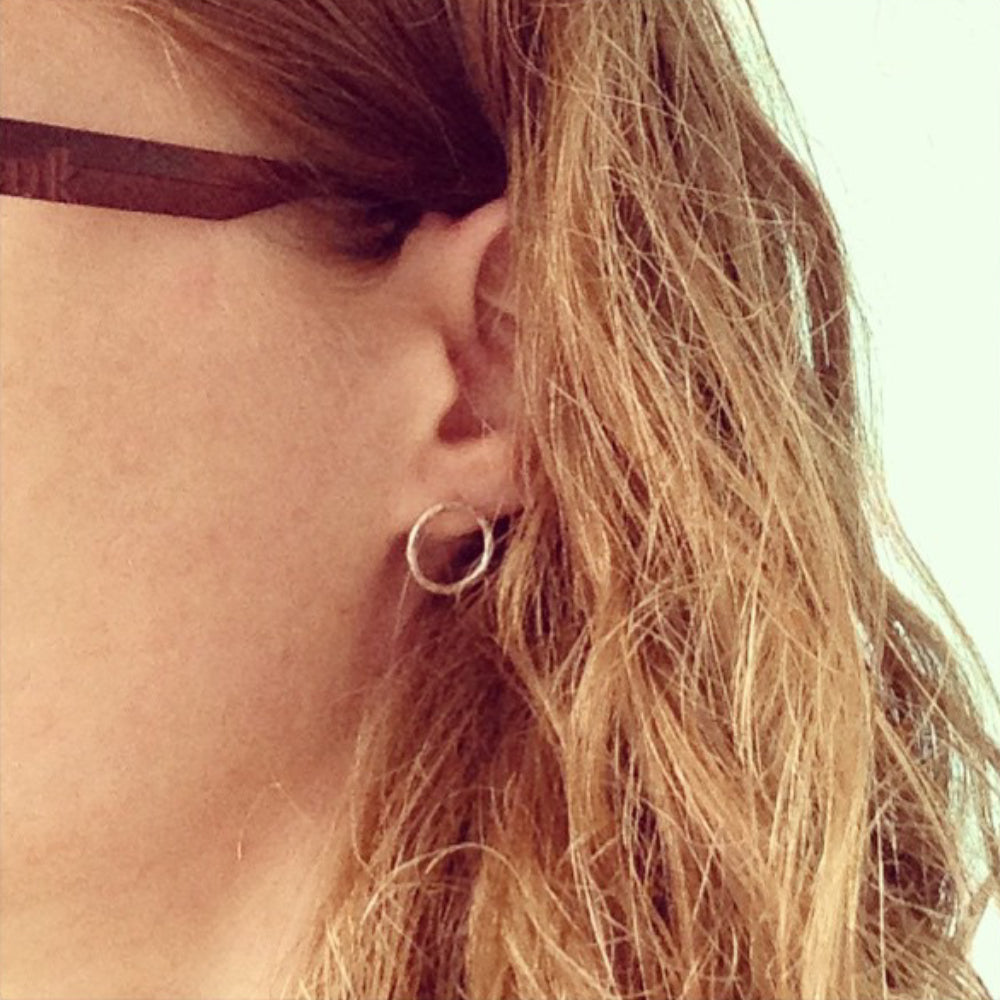 Showing a pair of stud earrings in silver wire formed into a circle outline and hammered to catch the light, being worn by zoe ruth designs.