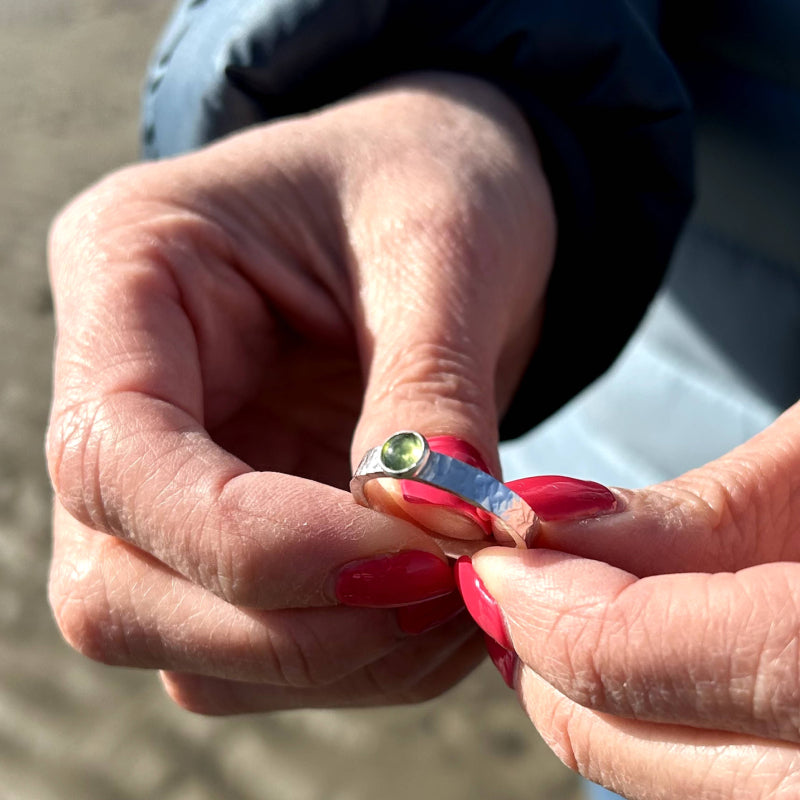 hands holding a green peridot and silver ring towards the sunlight