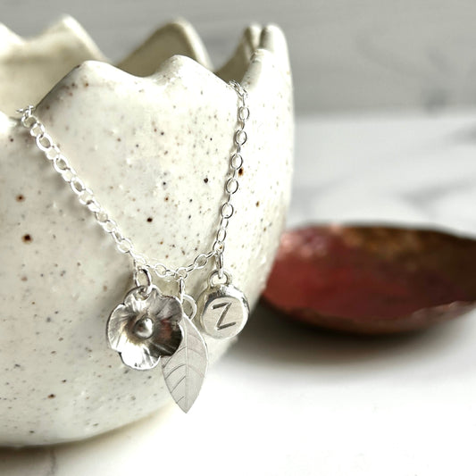 Silver charm necklace showing a handmade silver flower, leaf, and solid circle with letter Z stamped by zoe ruth designs