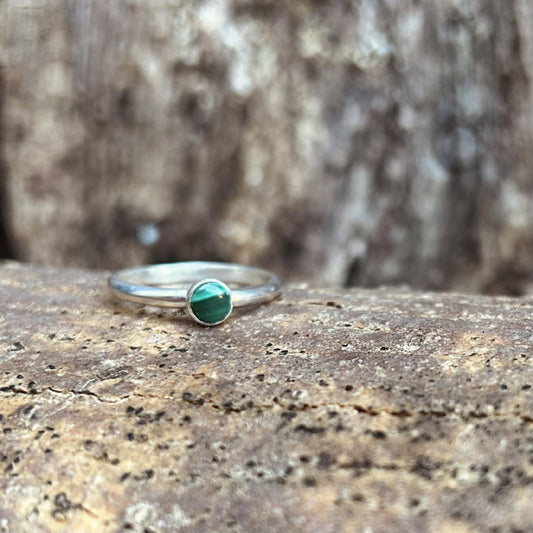A green banded malachite stone set in silvler on a silver smooth slim band ring, displayed sat on bark, by zoe ruth designs