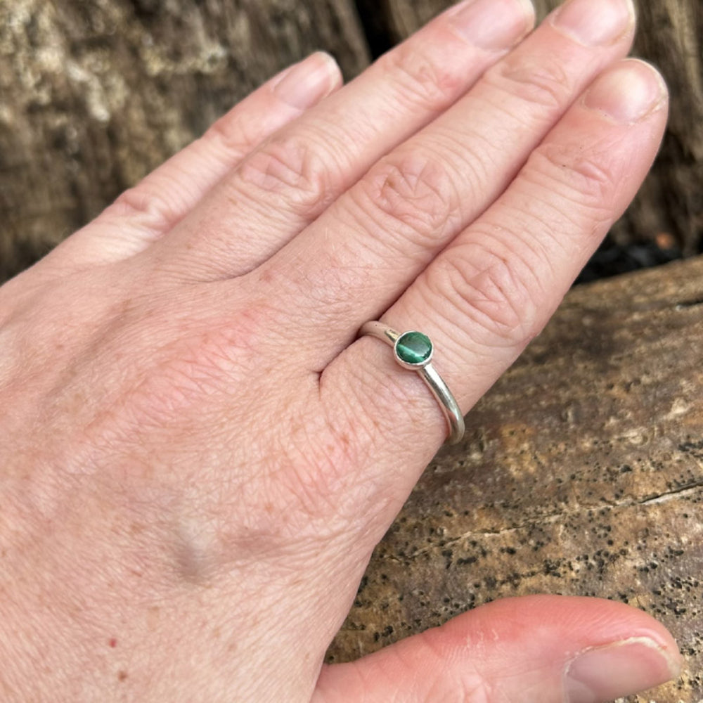 A green banded malachite stone set in silvler on a silver smooth slim band ring, displayed being worn on an index finger, by zoe ruth designs