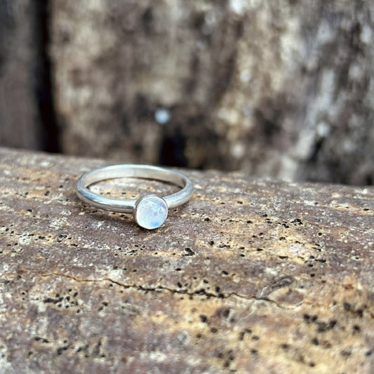 A moonstone ring set in silver on a smooth silver slim ring band displayed sat on tree bark, by zoe ruth designs