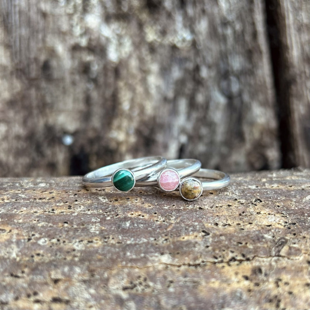 Three silver slim band smooth rings sat togehter each with a different stone, one a green malachite, one a pink rhodochrosite, one a brown picture jasper, by zoe ruth designs
